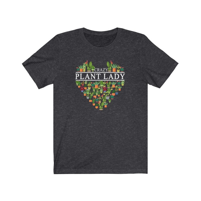 Puede incluir: Una camiseta gris oscuro jaspeada con un dise&ntilde;o en forma de coraz&oacute;n que presenta una variedad de plantas en macetas. El texto "Crazy Plant Lady" est&aacute; impreso en blanco sobre el coraz&oacute;n.