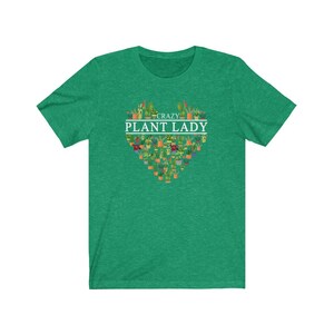 Puede incluir: Camiseta verde de manga corta con un dise&ntilde;o blanco en forma de coraz&oacute;n con el texto "Crazy Plant Lady" y una variedad de plantas en macetas.