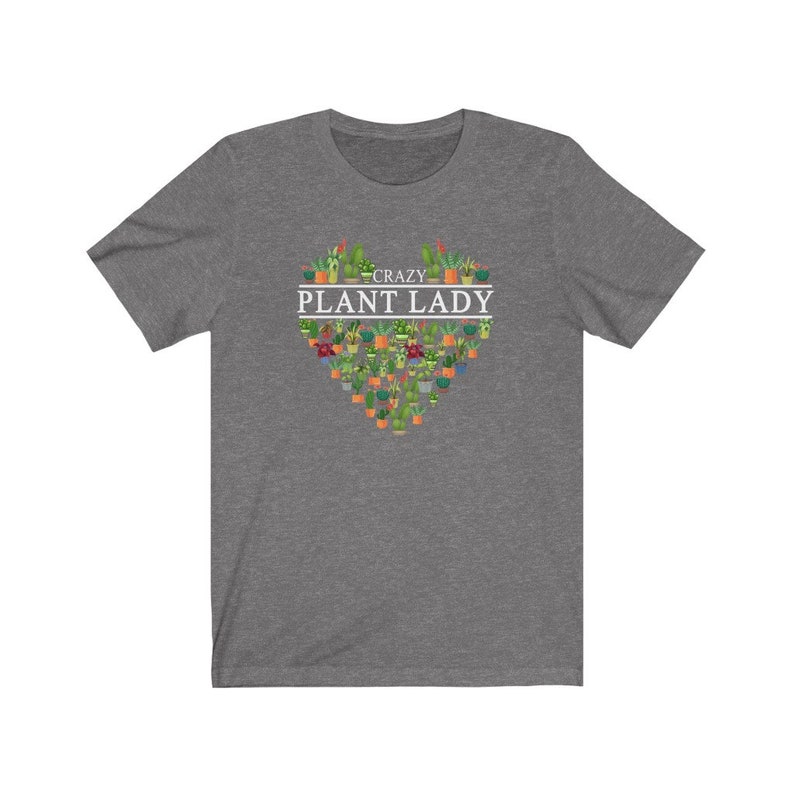 Puede incluir: Una camiseta gris jaspeada con un dise&ntilde;o en forma de coraz&oacute;n hecho de plantas en macetas. El texto "Crazy Plant Lady" est&aacute; impreso en blanco sobre el coraz&oacute;n.