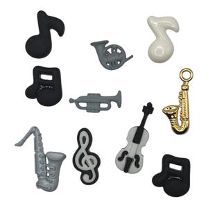 May include: A collection of musical instrument and music note charms in various colors. Includes a gold saxophone, a white and black violin, and gray trumpet and saxophone charms. Also features black and white treble clef and black music note charms.