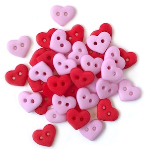 May include: A pile of heart-shaped buttons in pink and red. The buttons have two holes each.