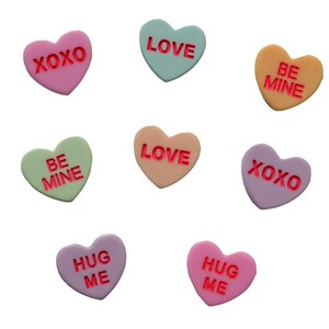 May include: A collection of colorful heart-shaped candies with various messages in red. The candies are in shades of pink, green, yellow, and purple, with phrases like "XOXO," "LOVE," "BE MINE," and "HUG ME" embossed on them. The candies are arranged against a white background.