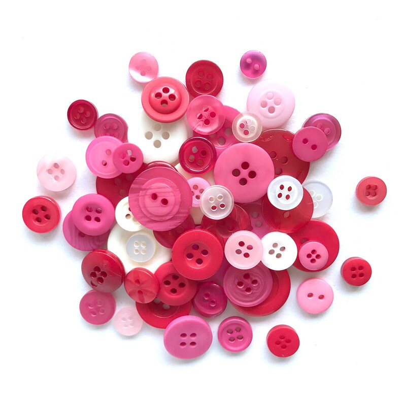 May include: A collection of pink and red buttons of various sizes and shapes. The buttons are made of plastic and have a glossy finish.