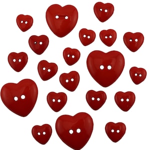 May include: A selection of glossy red heart-shaped buttons, each with two holes. The buttons are in various sizes and are arranged on a white backdrop. These decorative buttons are ideal for sewing and craft projects.