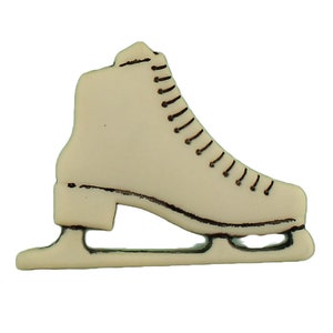 May include: A white plastic ice skate button with a brown outline. The button is shaped like a traditional ice skate with a blade and a boot.
