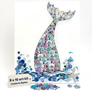 May include: A mixed media art kit featuring a mermaid tail design. The tail is crafted from various buttons in shades of blue, purple, and teal. The artwork includes embellishments like sequins, a starfish, and the text "8 x 10 art kit Create & display."