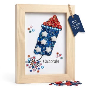 May include: A framed DIY craft kit featuring a firework design made of red, white, and blue buttons and star embellishments. The word "Celebrate" is written below the firework. A blue tag with "DIY CRAFT KIT" hangs from the frame.