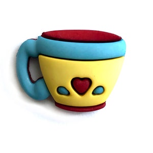 May include: A yellow teacup with a red heart and blue accents. The teacup has a red rim and a blue handle.