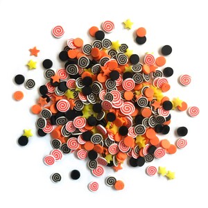 Op de afbeelding: Een hoop kleurrijke sprinkles in oranje, zwart en geel. De sprinkles zijn in de vorm van sterren en swirls.