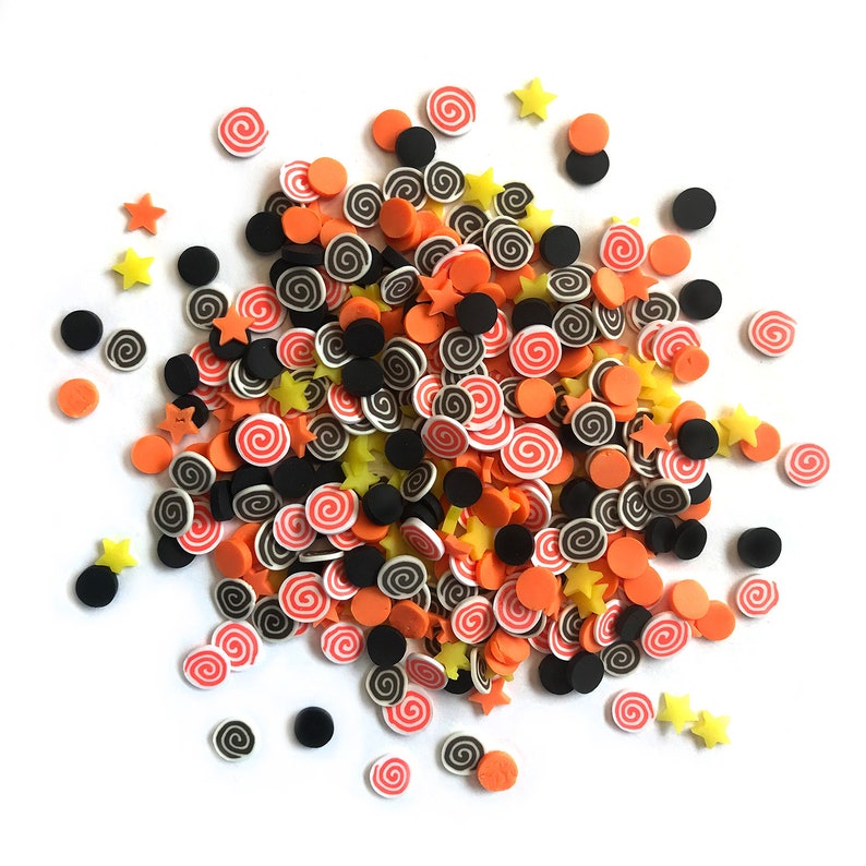 Op de afbeelding: Een hoop kleurrijke sprinkles in oranje, zwart en geel. De sprinkles zijn in de vorm van sterren en swirls.