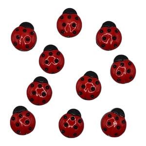 May include: Eleven red ladybug-shaped embellishments with black spots and black head caps are displayed against a white background. These decorative elements are ideal for craft projects.