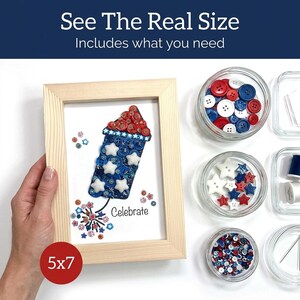 May include: A framed artwork featuring a firework design made of red, white, and blue buttons and star-shaped embellishments. The artwork is in a light wood frame and measures 5x7 inches. Additional craft supplies are displayed in small glass jars.