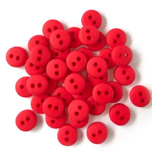 Op de afbeelding: Een verzameling kleine, ronde, felrode knopen met elk twee gaatjes. De knopen liggen verspreid op een witte ondergrond, wat een aantrekkelijke compositie oplevert. Ideaal voor naai- en knutselprojecten.