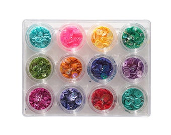 May include: A set of 12 small containers filled with colorful iridescent sequins. The containers are arranged in a clear plastic tray.