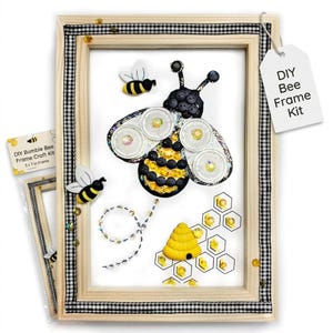 May include: DIY bee frame kit with a wooden frame, a gingham ribbon border, and a bee-themed design. The artwork includes a large bee made of buttons and sequins, a beehive, and honeycomb shapes. The frame is 5 x 7 inches.