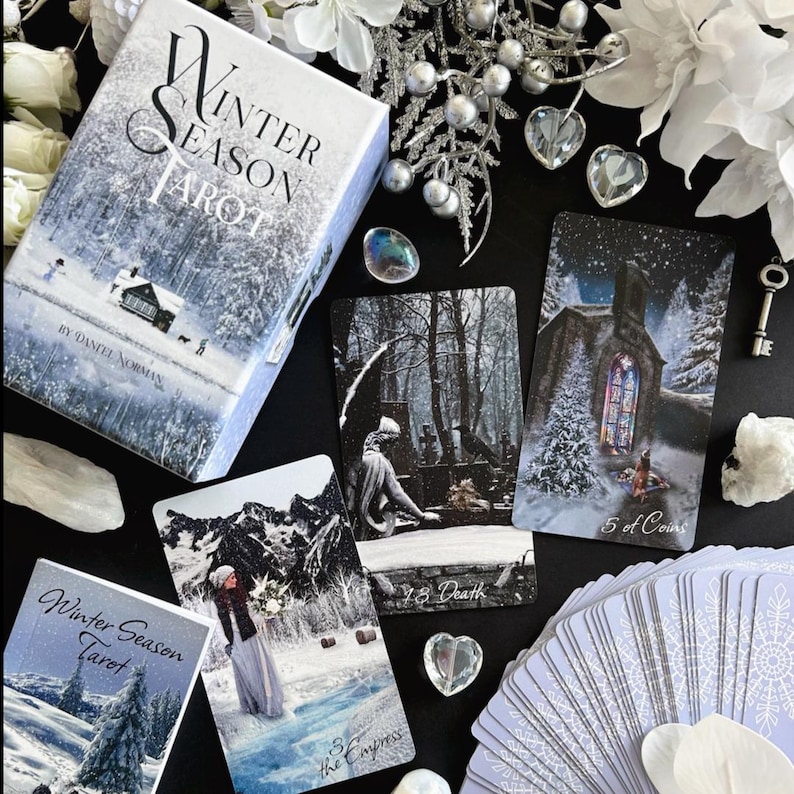 Peut inclure: Une bo&icirc;te de jeu de tarot "Winter Season Tarot" avec une sc&egrave;ne de for&ecirc;t enneig&eacute;e et le texte "Winter Season Tarot" sur le devant. La bo&icirc;te est ouverte et montre quelques cartes du jeu, dont la carte de la Mort et la carte 5 de pi&egrave;ces.