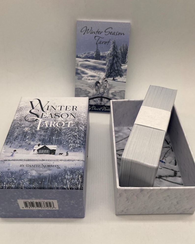 Peut inclure: Une bo&icirc;te de cartes de tarot Winter Season par Daniel Norman. La bo&icirc;te est bleue et blanche avec une sc&egrave;ne d'hiver sur le devant. La bo&icirc;te est ouverte et les cartes sont visibles &agrave; l'int&eacute;rieur.