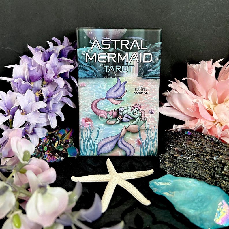 Puede incluir: Una carta de tarot con fondo negro y el texto "Astral Mermaid Tarot" en blanco. La carta presenta una ilustraci&oacute;n de dos sirenas con colas moradas y azules, nadando en un oc&eacute;ano turquesa con burbujas y algas marinas. El texto "by Daniel Norman" est&aacute; en blanco en la parte inferior de la carta.