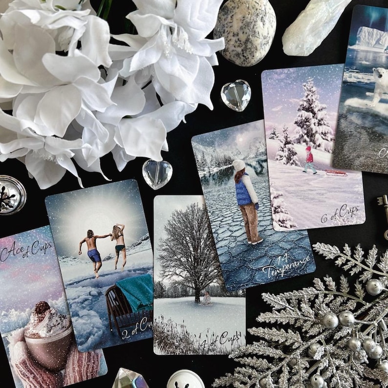 Peut inclure: Un jeu de cartes de tarot avec des images sur le th&egrave;me de l'hiver. Les cartes sont dispos&eacute;es sur une surface noire avec des fleurs blanches et des cristaux. Les cartes montrent des images d'un couple dans un paysage enneig&eacute;, d'un arbre dans un champ enneig&eacute;, d'une femme debout sur un chemin enneig&eacute; et d'une personne marchant sur un chemin enneig&eacute; avec un tra&icirc;neau.