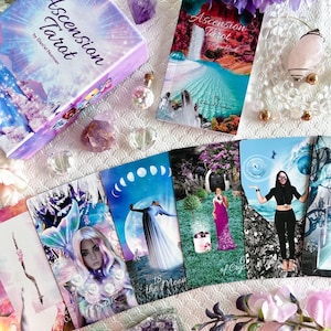 Puede incluir: Una baraja de tarot con una caja púrpura y blanca con el texto "Ascension Tarot" de Daniel Norman. Las cartas presentan ilustraciones coloridas con un tema celestial. Las cartas incluyen "La Luna" y "6 de Copas".