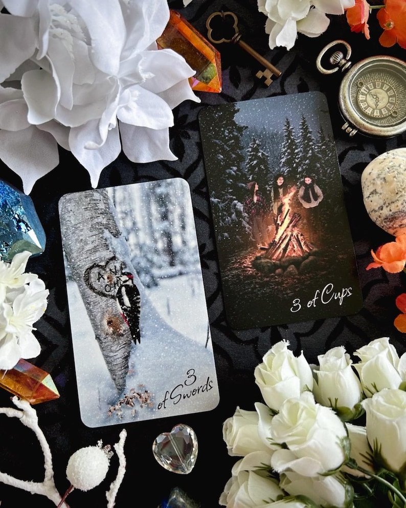 Peut inclure: Deux cartes de tarot, 3 d'&Eacute;p&eacute;es et 3 de Coupes, avec des sc&egrave;nes hivernales. La carte 3 d'&Eacute;p&eacute;es montre un pic sur un tronc d'arbre dans une for&ecirc;t enneig&eacute;e. La carte 3 de Coupes montre trois personnages r&eacute;unis autour d'un feu de joie dans une for&ecirc;t enneig&eacute;e.