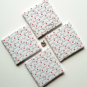 Puede incluir: Cuatro posavasos cuadrados blancos con un patrón rojo y negro de corazones y las palabras "live laugh love" repetidas.