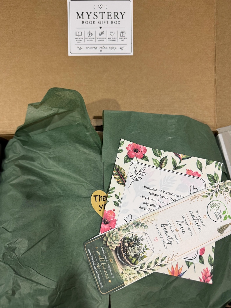Peut inclure: Une bo&icirc;te en carton ouverte avec du papier de soie vert et des cartes. Les cartes pr&eacute;sentent des motifs floraux et le texte "Mystery Book Gift Box". Une carte dit "Joyeux anniversaires aux amoureux des livres".
