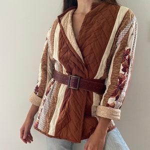 May include: A brown quilted jacket with a white and brown patterned design. The jacket has a wide collar and a belt.
