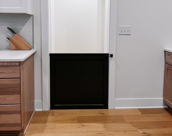 Può includere: Un cancelletto di sicurezza per bambini nero installato in una porta bianca con cornice bianca. Il cancelletto è chiuso e ha una maniglia bianca. Il pavimento è in legno marrone chiaro.