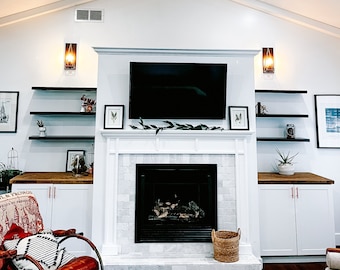 May include: A white fireplace with a black fireplace screen and a white marble surround. The fireplace is flanked by white cabinets with wood countertops. There are shelves above the cabinets with decorative items.