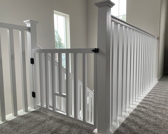 May include: White wooden baby gate with a modern design, installed at the top of a staircase. The gate has a white painted finish and black hardware.