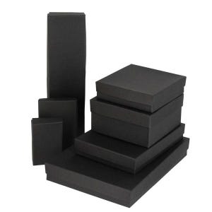 Può includere: Una collezione di scatole di cartone nere di varie dimensioni. Le scatole sono rettangolari e quadrate, con coperchi. Le scatole sono impilate e disposte per mostrare le diverse dimensioni. Le scatole sono tutte di colore nero opaco.
