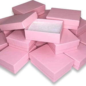 May include: A collection of pink rectangular gift boxes, some open to reveal a white interior. The boxes are stacked and arranged, creating a visually appealing display. The boxes are a soft, pastel pink color.