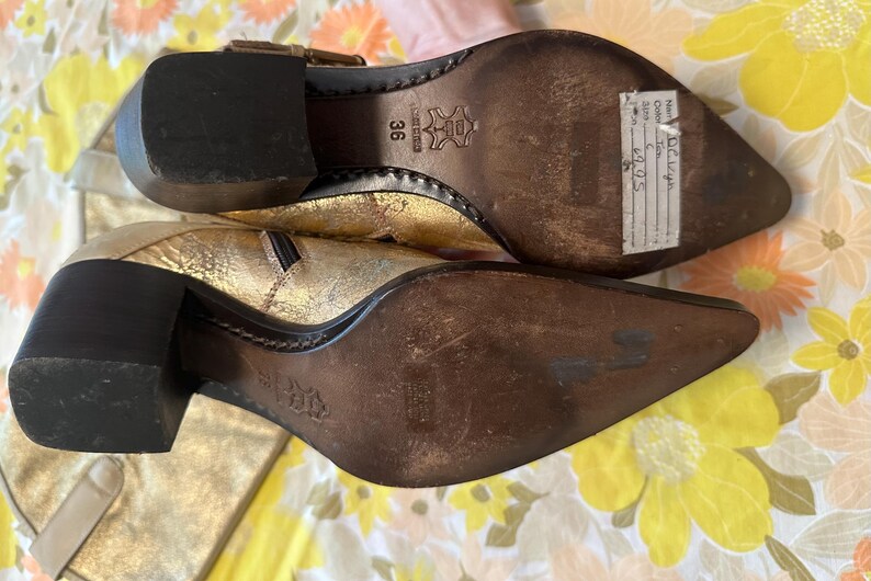 Puede incluir: Botines dorados con tac&oacute;n de bloque. Los botines tienen punta afilada y cremallera lateral. Las suelas son marrones y el tac&oacute;n mide unos 5 cm de alto.