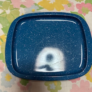 Puede incluir: Una bandeja de esmalte azul con un patrón blanco moteado. La bandeja tiene esquinas redondeadas y un borde elevado. La bandeja está vacía y parece ser vintage.