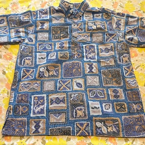 May include: Short-sleeved button-down shirt with a blue background and a repeating pattern of geometric shapes in shades of blue, brown, and white. The shirt has a collar and a buttoned placket.