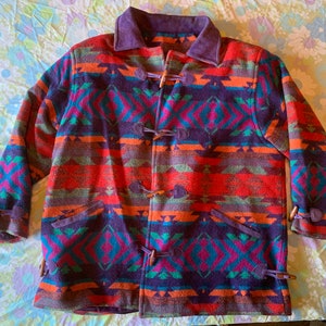 Może przedstawiać: Kolorowa, wielokolorowa kurtka w stylu południowo-zachodnim z brązowym kołnierzem ze skóry zamszowej i drewnianymi zapięciami.