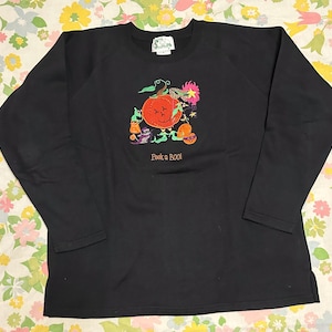 May include: Black long-sleeved sweatshirt with a colorful embroidered Halloween design. The design features a smiling orange pumpkin, ghosts, and the text "Peek a Boo!" in a playful font. The sweatshirt has a crew neck and raglan sleeves.