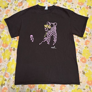 Pu&ograve; includere: Una maglietta marrone con un ghepardo rosa che indossa occhiali da sole e la scritta "cool cat" stampata sul davanti. La maglietta ha un piccolo logo che dice "get outside nature" nell'angolo in basso a destra.