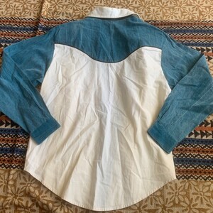 May include: A long-sleeved shirt with a white body and blue sleeves and yoke. The shirt has a button-down collar and a curved yoke design. The sleeves and yoke are a textured blue fabric, while the body is a smooth white fabric.