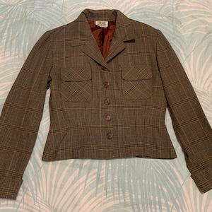 May include: A brown and tan plaid blazer with a button front and two flap pockets. The blazer has a fitted waist and long sleeves with button cuffs.