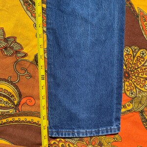 Puede incluir: Primer plano de la parte inferior de un par de pantalones vaqueros azules. Se puede ver una cinta m&eacute;trica en el lado izquierdo de la imagen.