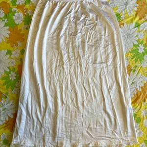 May include: A white slip skirt with a lace trim. The skirt is made of a silky material and has a smooth, flowing texture.