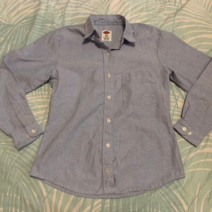 May include: A light blue long-sleeved button-down shirt with a single chest pocket. The shirt has a standard collar and a button closure.