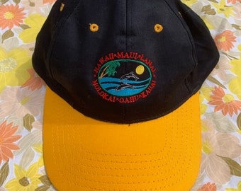Può includere: Cappellino da baseball nero e giallo con un logo ricamato che dice "Hawaii Maui Lanai Molokai Oahu Kauai".