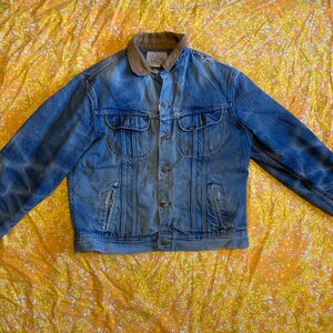 Op de afbeelding: Een blauw denim jack met een bruine corduroy kraag. Het jack heeft een knoopsluiting en twee voorzakken.