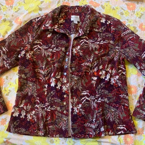 May include: A long-sleeved button-up shirt with a red, white, and green floral pattern. The shirt has a collared neckline and a button-up front.