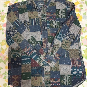 Könnte beinhalten: Ein Hemd mit Knopfleiste und Patchwork-Design in Blau-, Grün-, Braun- und Burgundertönen. Das Hemd weist verschiedene geometrische und Paisley-Muster auf. Der Kragen trägt die Marke "Woolrich".