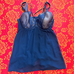 Puede incluir: Conjunto de lencería babydoll azul marino. La parte superior presenta una tela transparente y fluida con un sujetador incorporado. Las copas del sujetador son de color beige claro con detalles de encaje azul marino. Las correas son finas y ajustables.