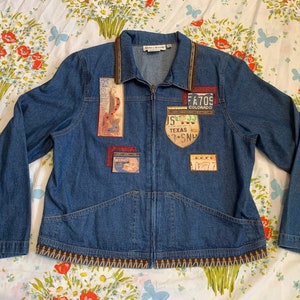 May include: A blue denim jacket with a zipper closure and various patches. Patches include a guitar, license plates, and other designs. The collar and hem are trimmed with a brown and tan patterned design.
